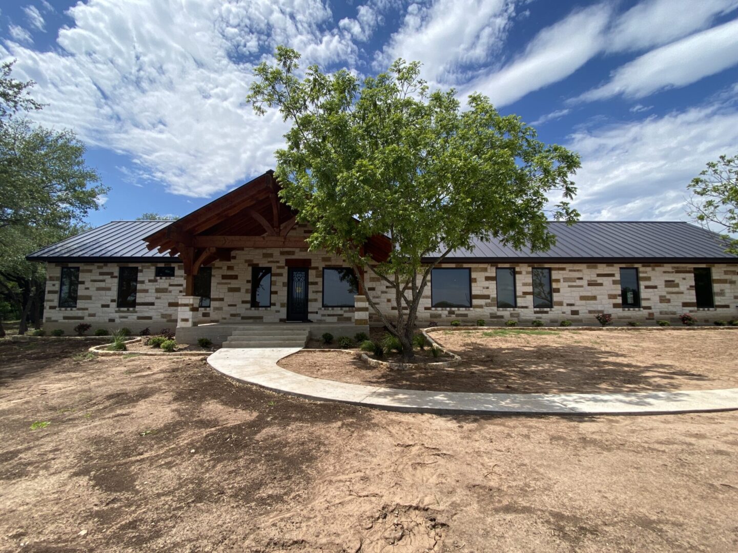 Stone house with a black roof and a tree in the front yard.